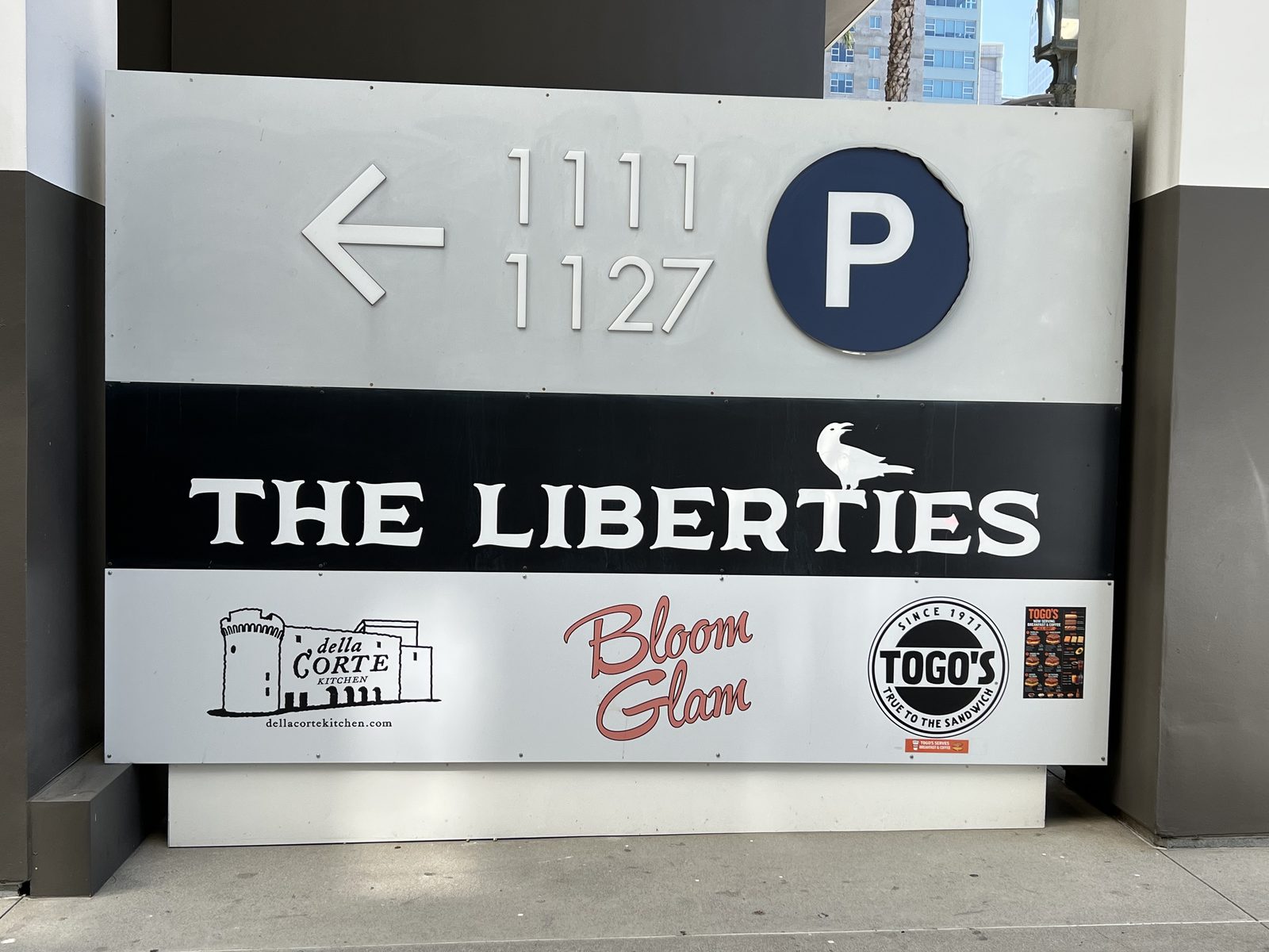 The driveway sign for 1111 and 1127 Wilshire Boulevard, marked with a parking symbol and the names of the building's ground-floor businesses