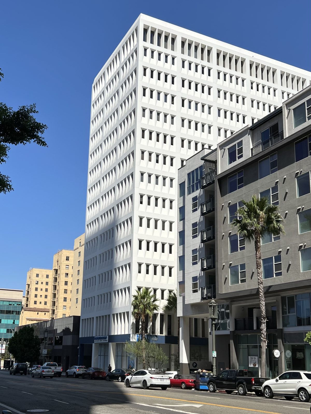1127 Wilshire Boulevard seen along the street, with palm trees and traffic in front of it