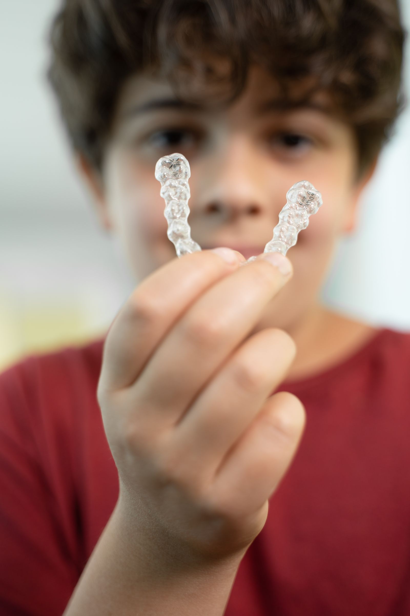A teenage patient holding a pair of clear aligners